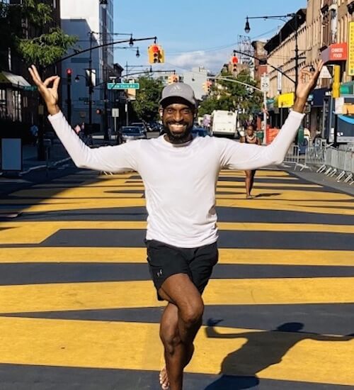 Derric Harris, yoga and meditation teacher, smiling during Garudasana (Eagle’s Pose) on a public street