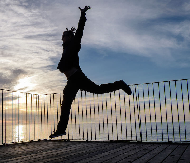 A person leaping on the Esalen pool deck against the backdrop of sunset over the Pacific ocean. Photo credit: Melina Meza